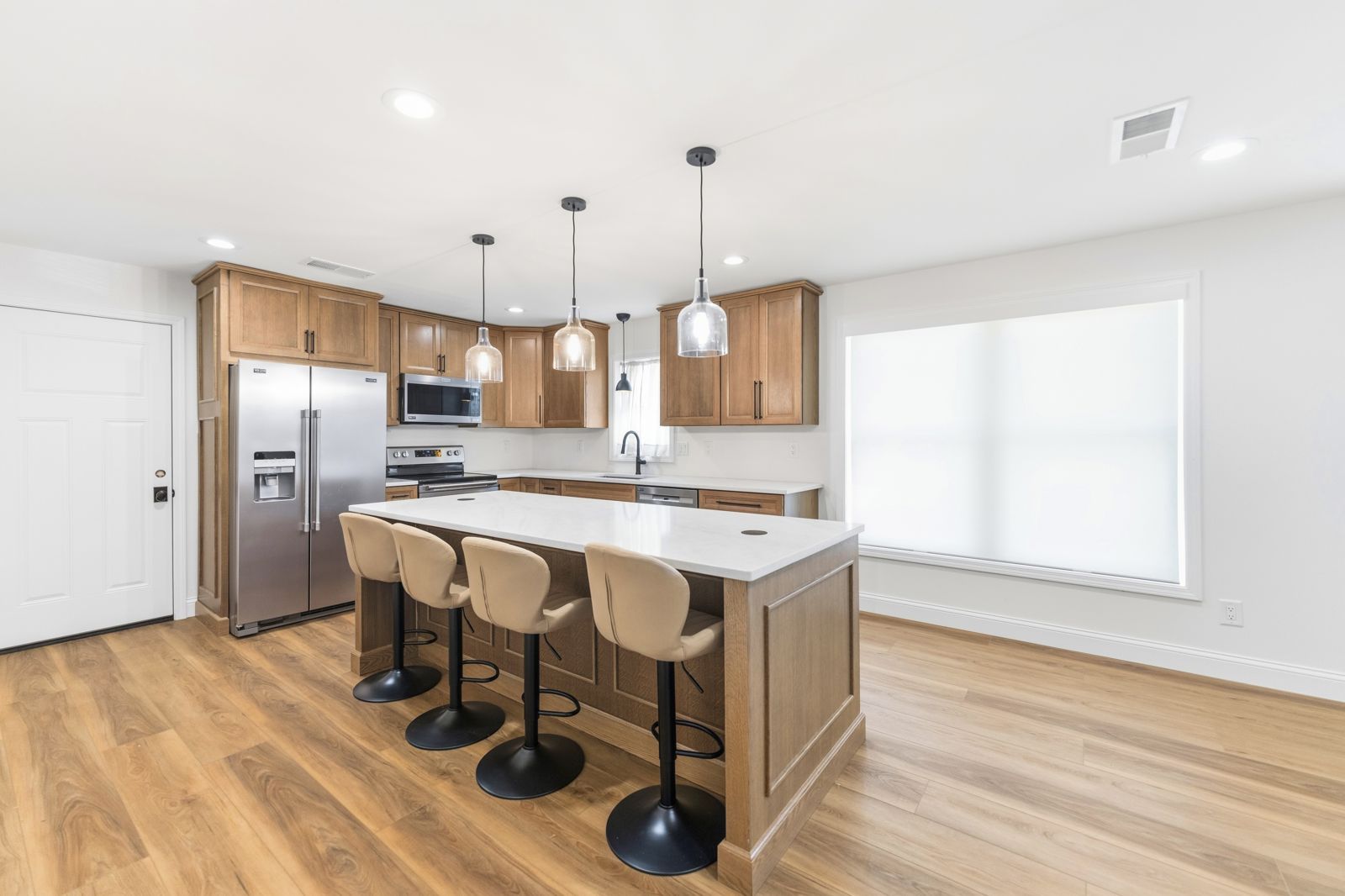 Oak kitchen with large island, cream bar stools, and glass pendants